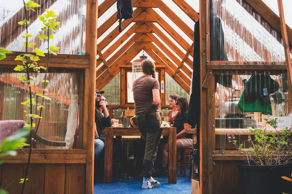 Residency guests gathered around a long table in a timber-framed greenhouse while Lori McCarthy leads the session